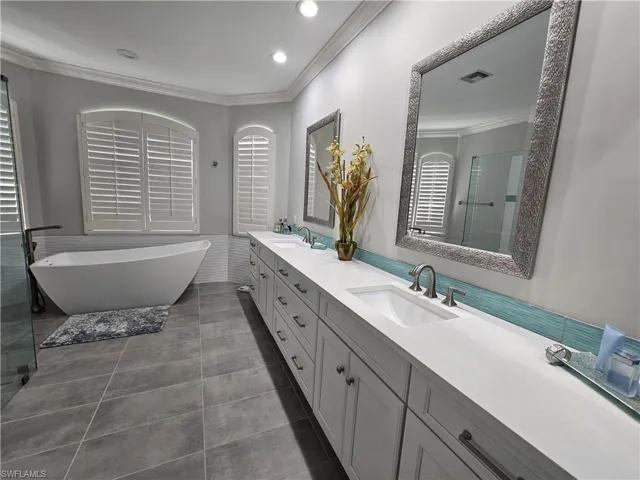 Bathroom with crown molding, double vanity, a freestanding bath, recessed lighting, and dark tile patterned floors