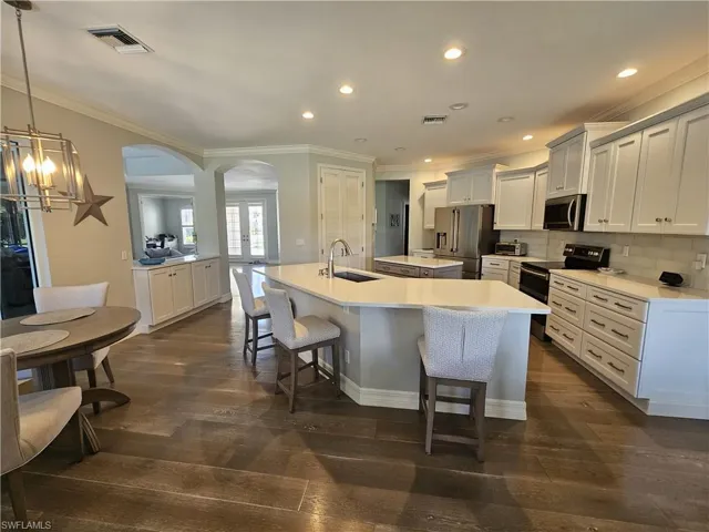 Kitchen featuring stainless steel appliances, ornamental molding, a kitchen bar, decorative backsplash, and dark wood-type flooring