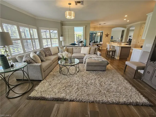 Living room featuring dark wood-style flooring, crown molding, arched walkways, and recessed lighting
