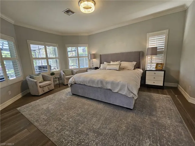 Bedroom with dark wood-style floors, multiple windows, and ornamental molding