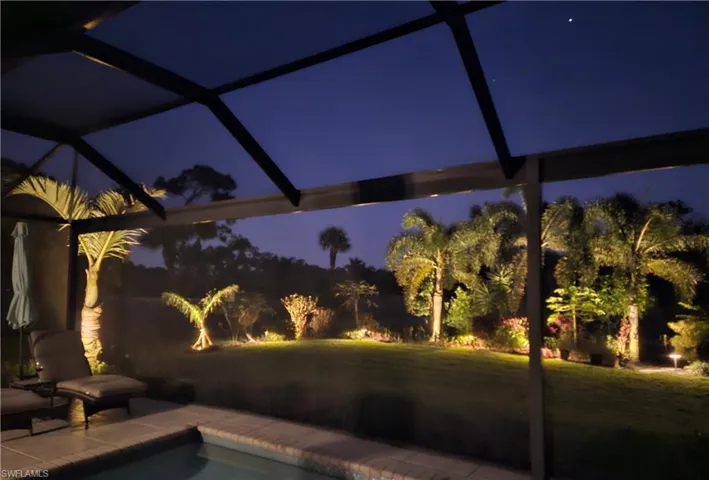 Pool at night featuring a lawn, a lanai, an outdoor pool, and a patio
