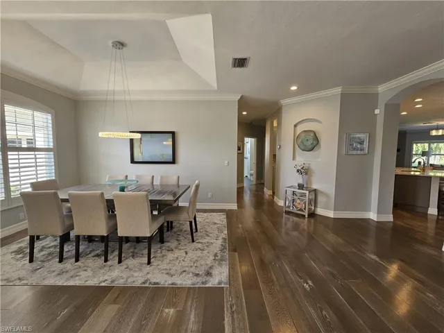 Dining area with dark wood finished floors, recessed lighting, arched walkways, a tray ceiling, and ornamental molding