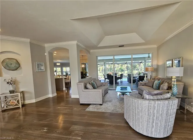 Living area with crown molding, arched walkways, dark wood-type flooring, and a tray ceiling