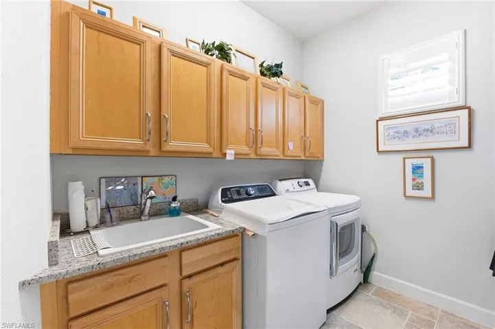 Laundry room with washing machine and dryer, cabinet space, and light stone finish floors