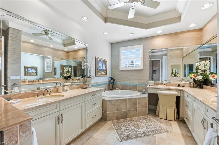 Full bathroom with ornamental molding, a ceiling fan, a garden tub, two vanities, and a raised ceiling