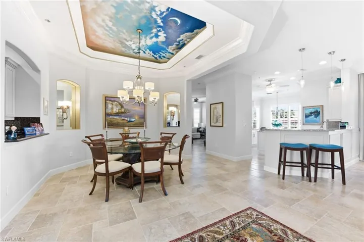 Dining area featuring crown molding, ceiling fan, hanging lights, light stone finish floors, and a tray ceiling