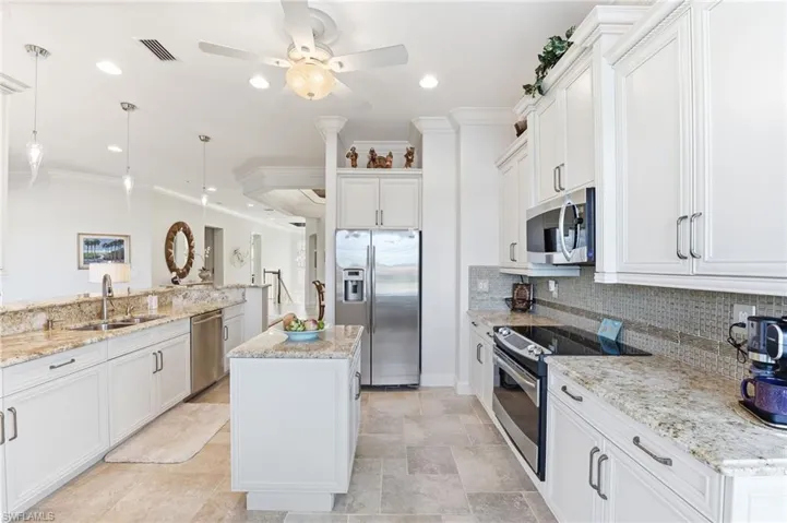 Kitchen with crown molding, stainless steel appliances, decorative light fixtures, a center island, and white cabinetry