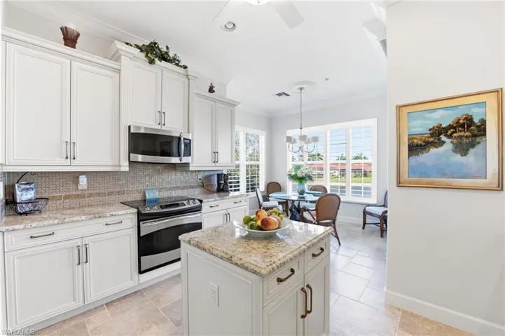 Kitchen featuring crown molding, white cabinetry, stainless steel appliances, light stone counters, and ceiling fan