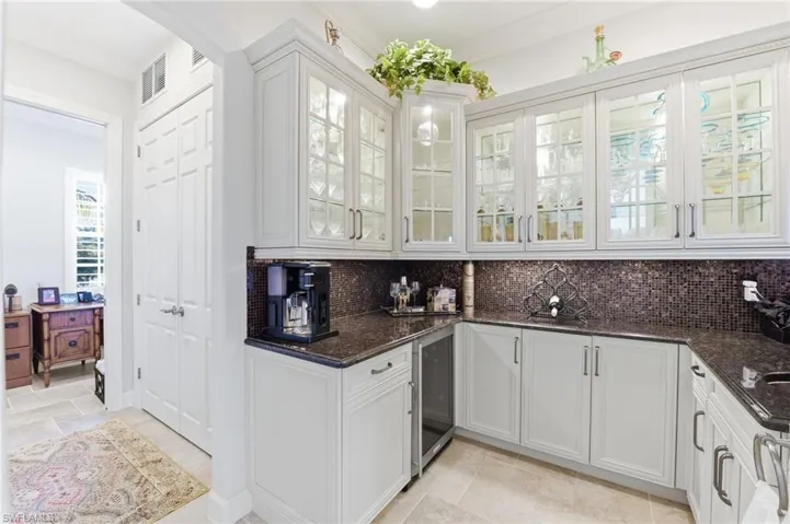 Bar area with white cabinetry, dark stone counters, glass insert cabinets, wine cooler, and decorative backsplash