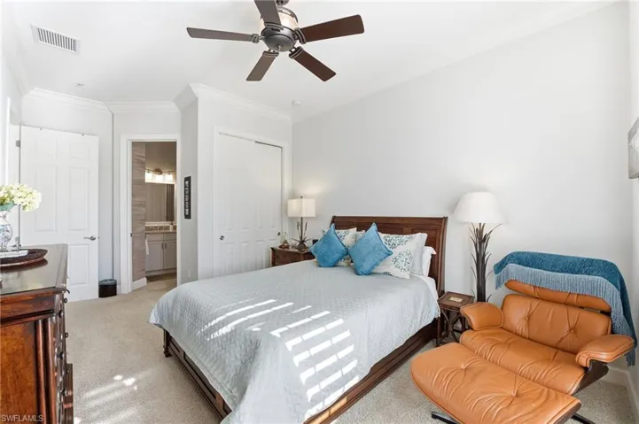 Carpeted bedroom with a closet, crown molding, ceiling fan, and ensuite bath