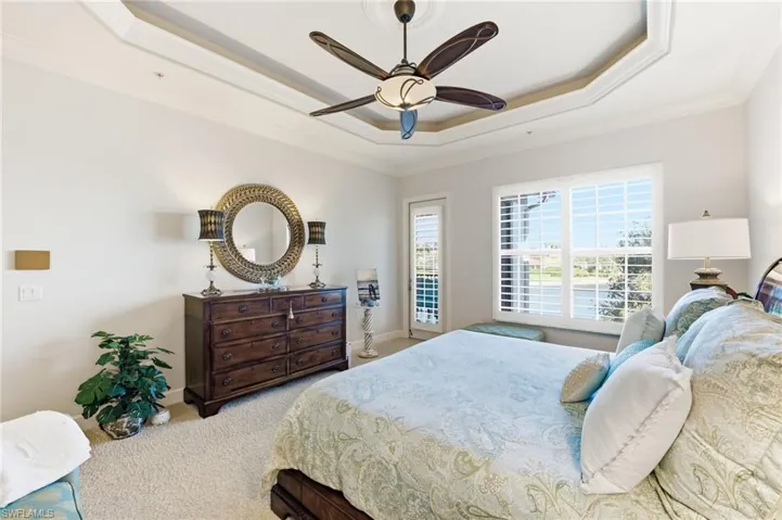 Carpeted bedroom featuring a ceiling fan, ornamental molding, and a raised ceiling