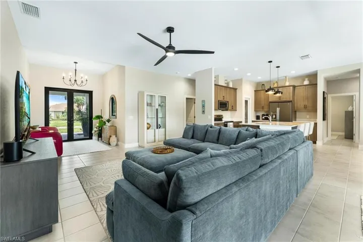 Tiled living room featuring ceiling fan with notable chandelier and french doors