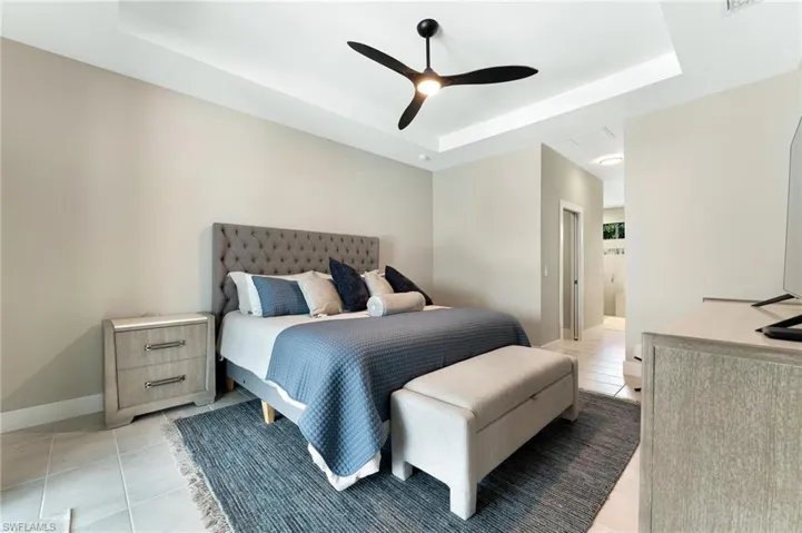 Tiled bedroom with a raised ceiling, ensuite bathroom, and ceiling fan