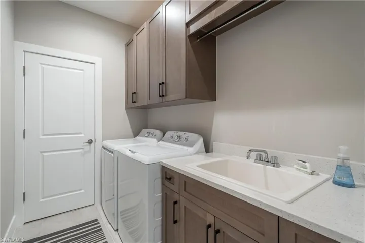 Clothes washing area featuring sink, cabinets, washer and dryer, and light tile patterned flooring