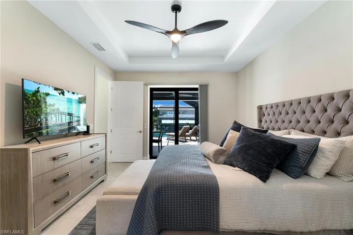 Tiled bedroom featuring ceiling fan, access to exterior, and a tray ceiling