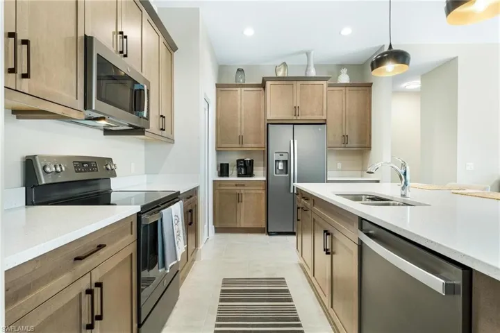 Kitchen with light tile patterned flooring, light stone counters, appliances with stainless steel finishes, pendant lighting, and sink