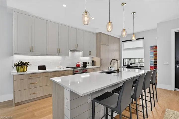 Kitchen featuring light stone countertops, light brown cabinetry, light wood-style flooring, hanging light fixtures, and a breakfast bar area