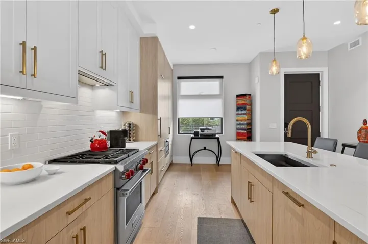 Kitchen featuring light brown cabinets, premium range, light stone counters, hanging light fixtures, and light wood-style floors