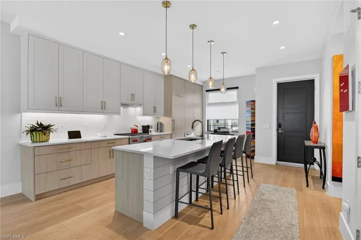Kitchen with light brown cabinetry, a kitchen breakfast bar, pendant lighting, light stone countertops, and a kitchen island with sink