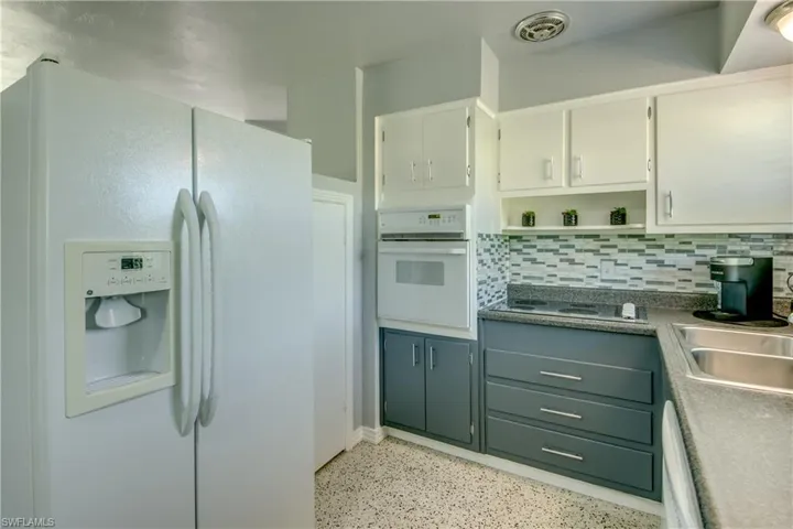 Kitchen featuring sink, white appliances, white cabinetry, and backsplash