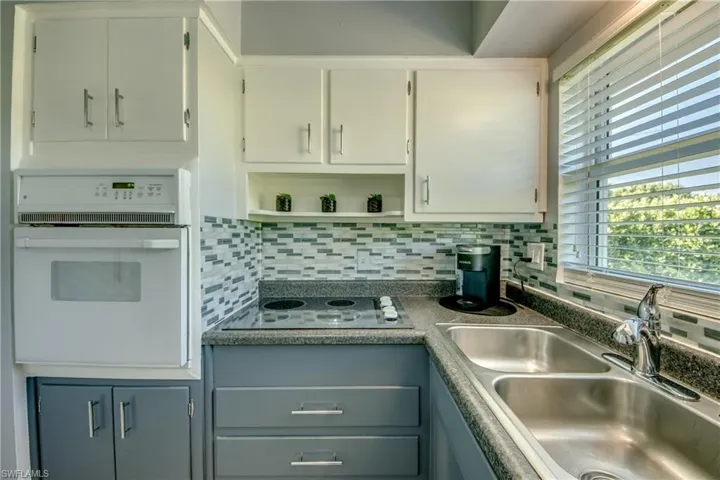 Kitchen with black electric stovetop, oven, tasteful backsplash, gray cabinets, and sink