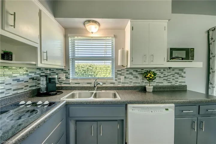 Kitchen featuring gray cabinetry, sink, white appliances, and backsplash