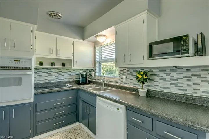 Kitchen featuring backsplash, sink, black appliances, and white cabinetry