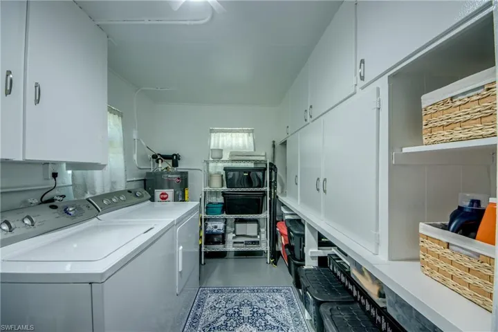Laundry room with a healthy amount of sunlight, cabinets, washing machine and dryer, and electric water heater