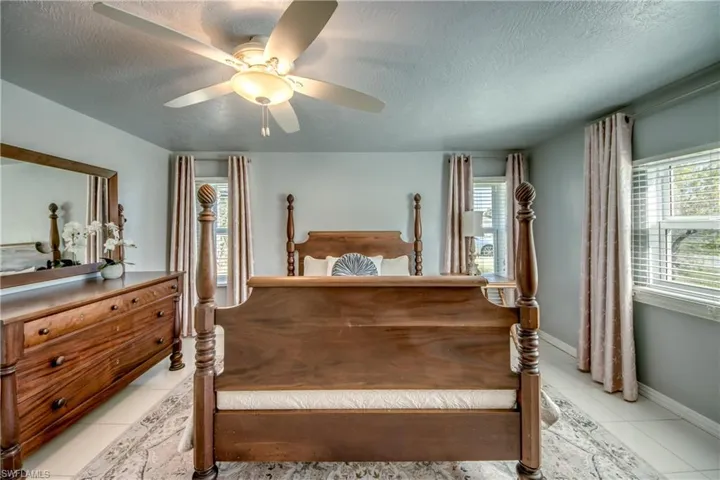 Bedroom with ceiling fan, a textured ceiling, and light tile floors
