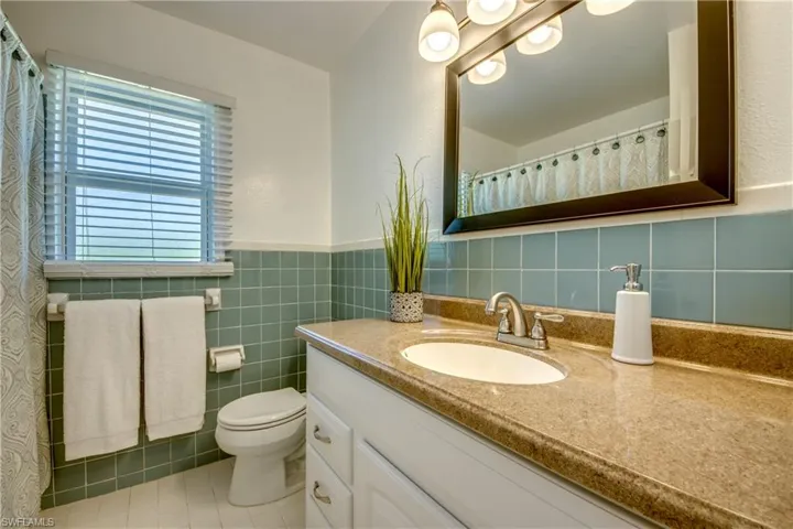 Bathroom featuring tile flooring, vanity with extensive cabinet space, tile walls, backsplash, and toilet