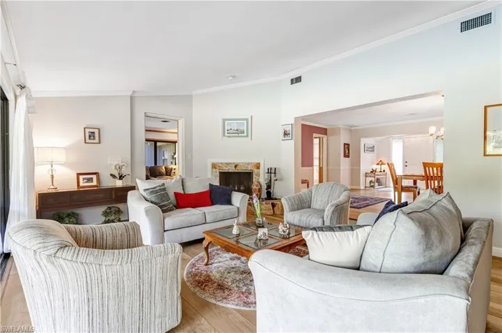 Living room featuring crown molding, vaulted ceiling, wood finished floors, a chandelier, and a stone fireplace