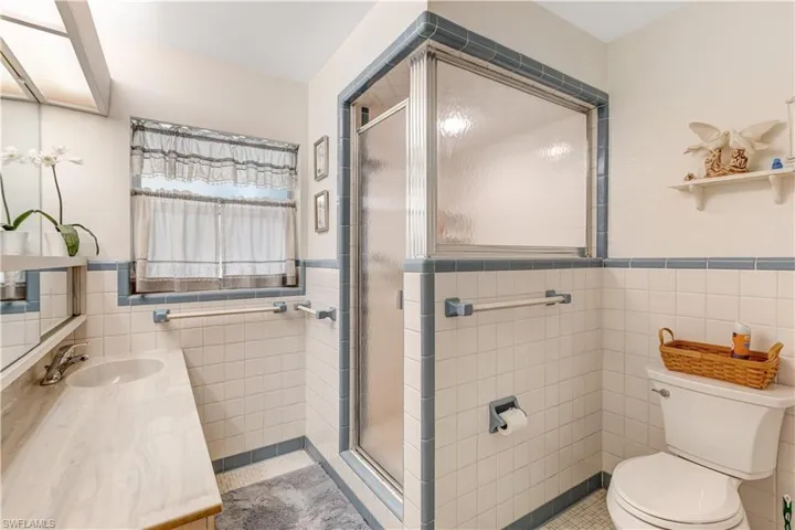 Bathroom featuring tile walls, vanity, wainscoting, a stall shower, and light tile patterned floors
