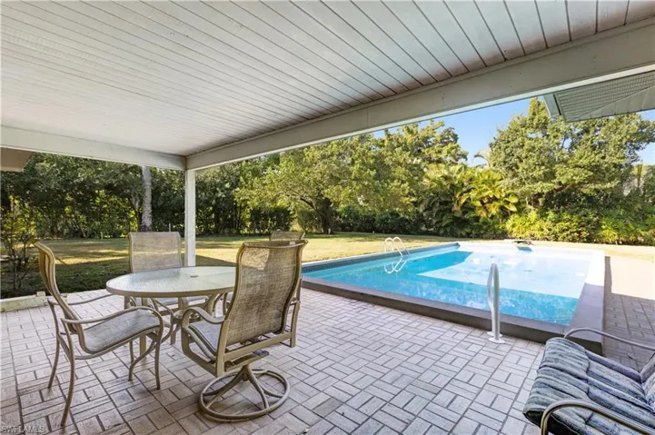 Swimming pool featuring outdoor dining space, a lawn, a patio area, and view of scattered trees
