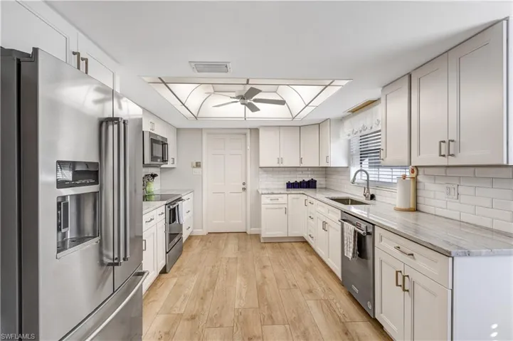 Kitchen with stainless steel appliances, light stone countertops, light wood-type flooring, backsplash, and white cabinets