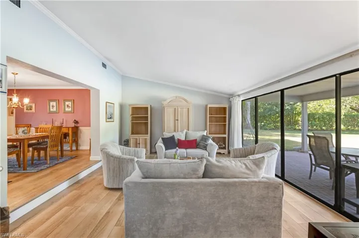 Living area featuring lofted ceiling, ornamental molding, light wood-style flooring, and a chandelier