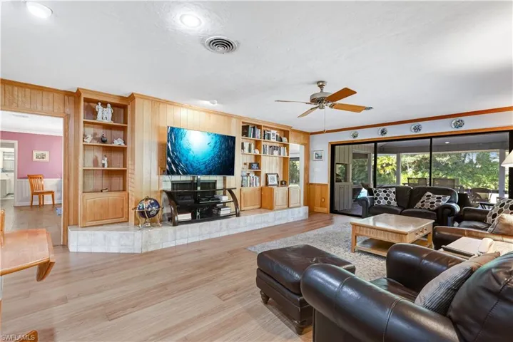 Living area with built in shelves, ornamental molding, ceiling fan, wooden walls, and wood finished floors