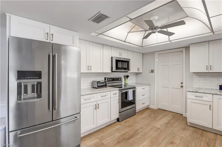Kitchen with appliances with stainless steel finishes, white cabinetry, light wood-style flooring, ceiling fan, and tasteful backsplash