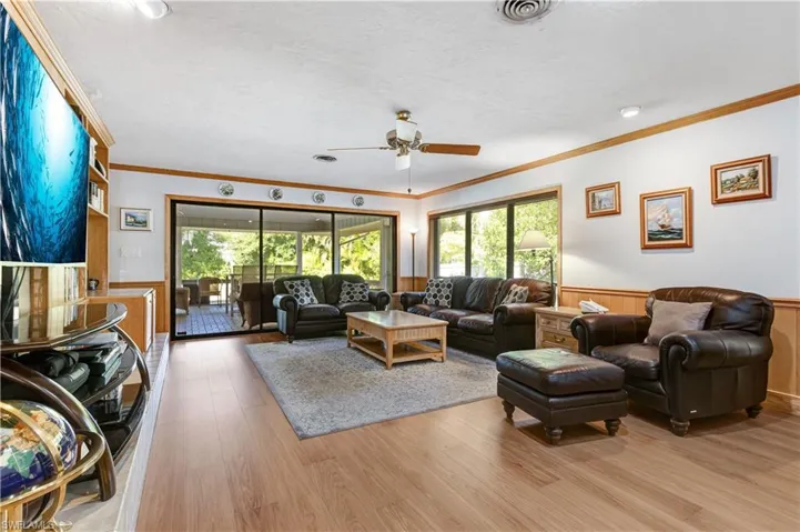 Living room with a wainscoted wall, plenty of natural light, light wood finished floors, a ceiling fan, and ornamental molding