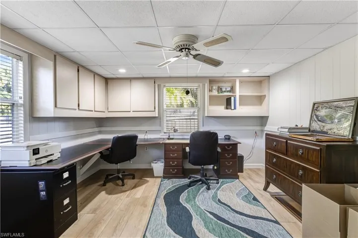 Office space with ceiling fan, built in study area, light wood finished floors, and a drop ceiling