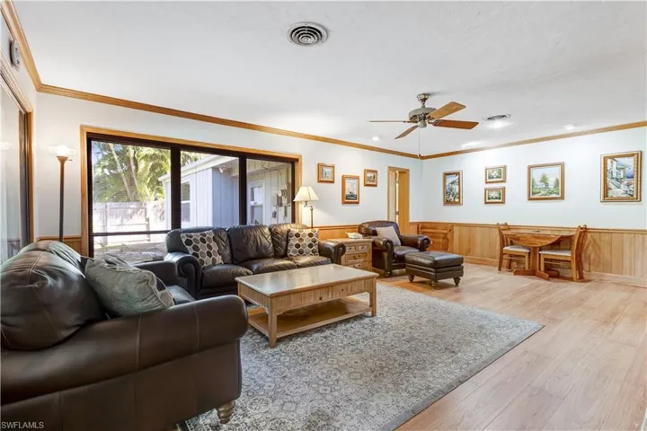 Living room with light wood-type flooring, wainscoting, ornamental molding, and ceiling fan