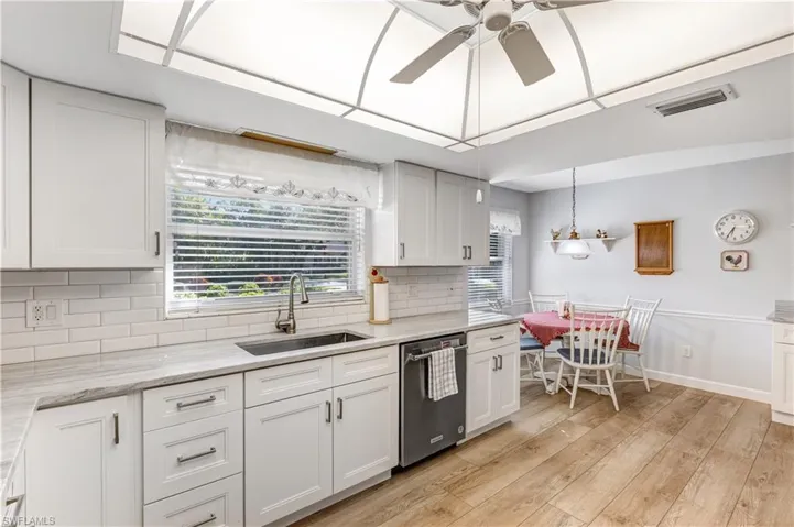 Kitchen with white cabinets, decorative backsplash, dishwasher, light wood finished floors, and a ceiling fan