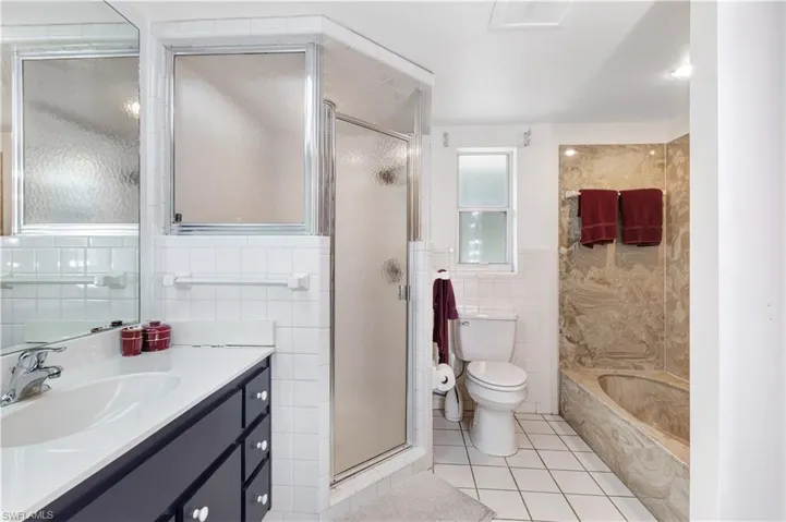 Full bath with tile walls, vanity, light tile patterned flooring, a garden tub, and a stall shower