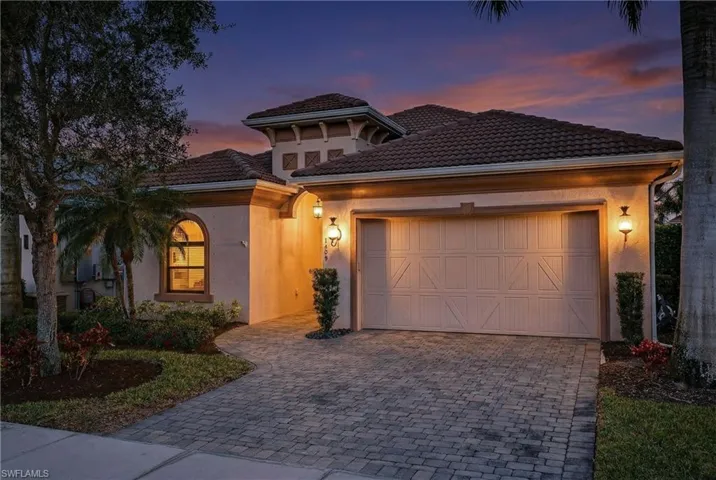 Naples Florida pool home at sunset with two-car garage, paver driveway, tile roof, and manicured landscaping in preferred X500 flood zone