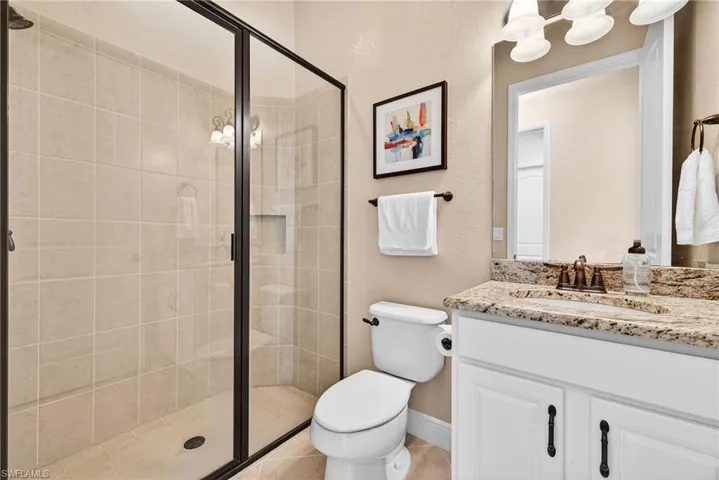 Guest bathroom immediately adjacent to guest bedroom with quartz vanity, walk-in glass-enclosed shower, and contemporary finishes
