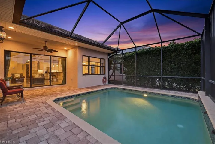 Southwestern-exposure screened lanai at sunset featuring heated pool, water features, lake views, and enhanced tropical landscaping for privacy