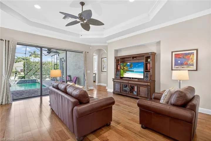 Living area with tray ceiling, crown molding, ceiling fan, light hardwood floors, and impact sliding glass doors opening to the covered lanai and pool