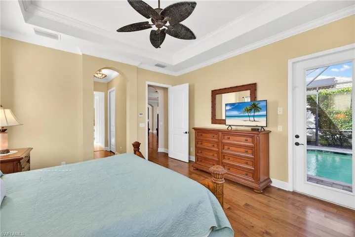 Bedroom with engineered hardwood flooring, crown molding, and tray ceiling with ceiling fan