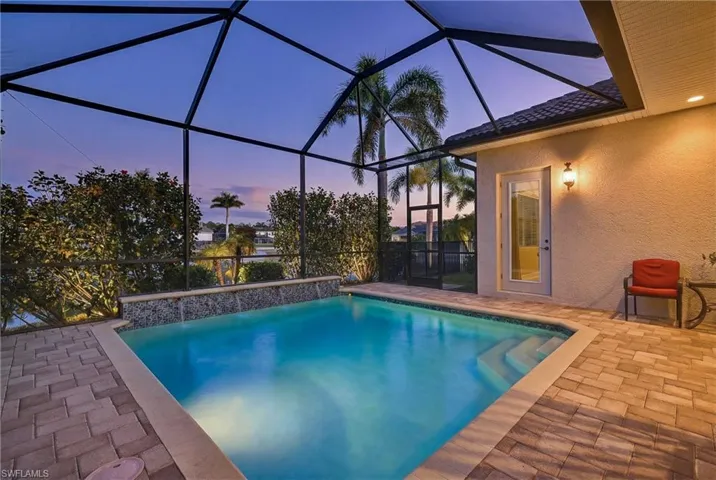 Southwestern-exposure screened lanai at sunset featuring heated pool, water features, lake views, and enhanced tropical landscaping for privacy