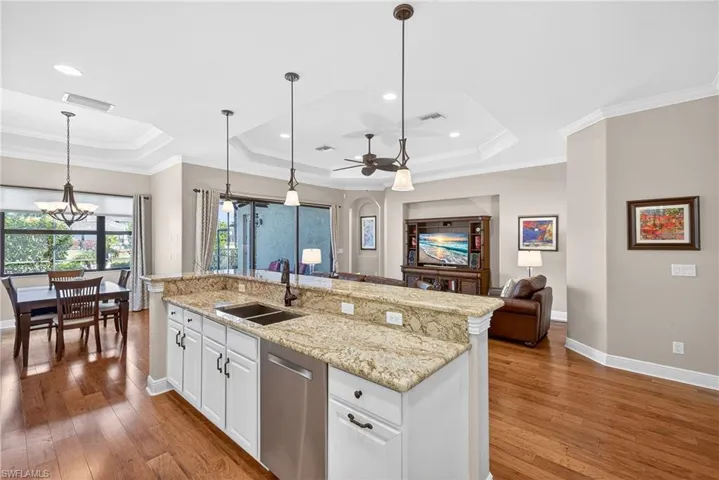 Open kitchen featuring pendant lighting, white cabinetry, stainless steel appliances, crown molding, and new granite countertops, and glass impact doors to lanai