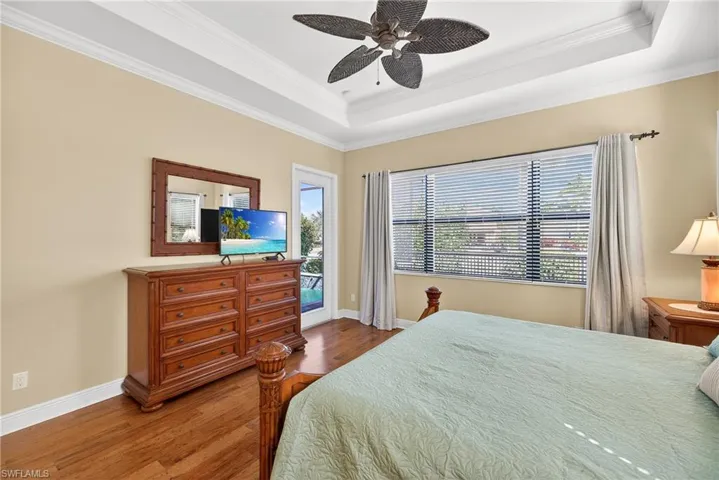 Bedroom with engineered hardwood flooring, crown molding, tray ceiling, a ceiling fan, and lake views
